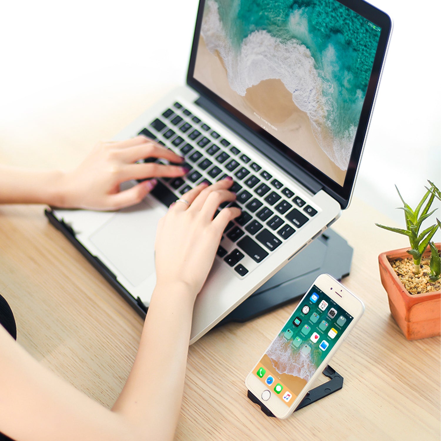 Female typing on laptop raised on black stand,.  iPhone neatly stood in stand next to laptop. 