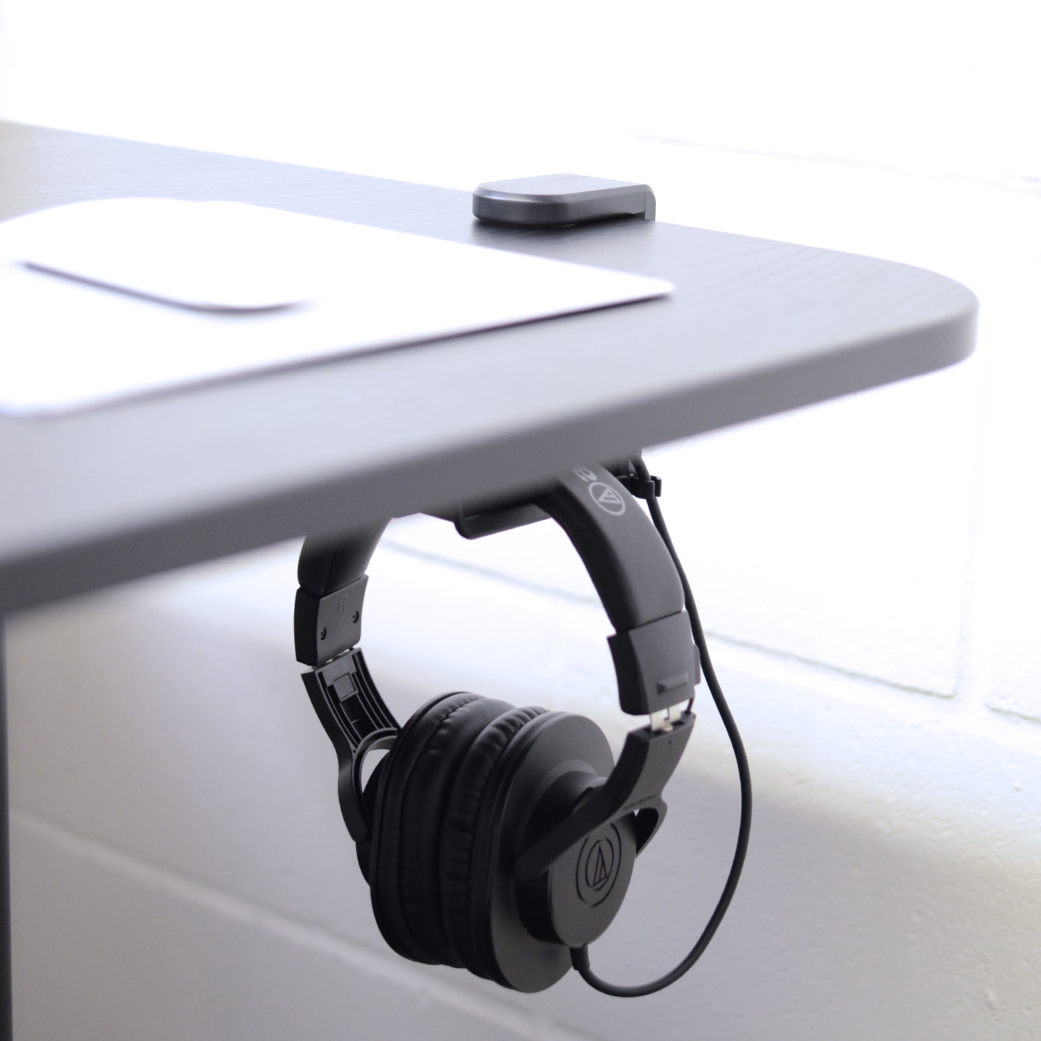 Black headphones on under desk headphone hanger attached to a white desk