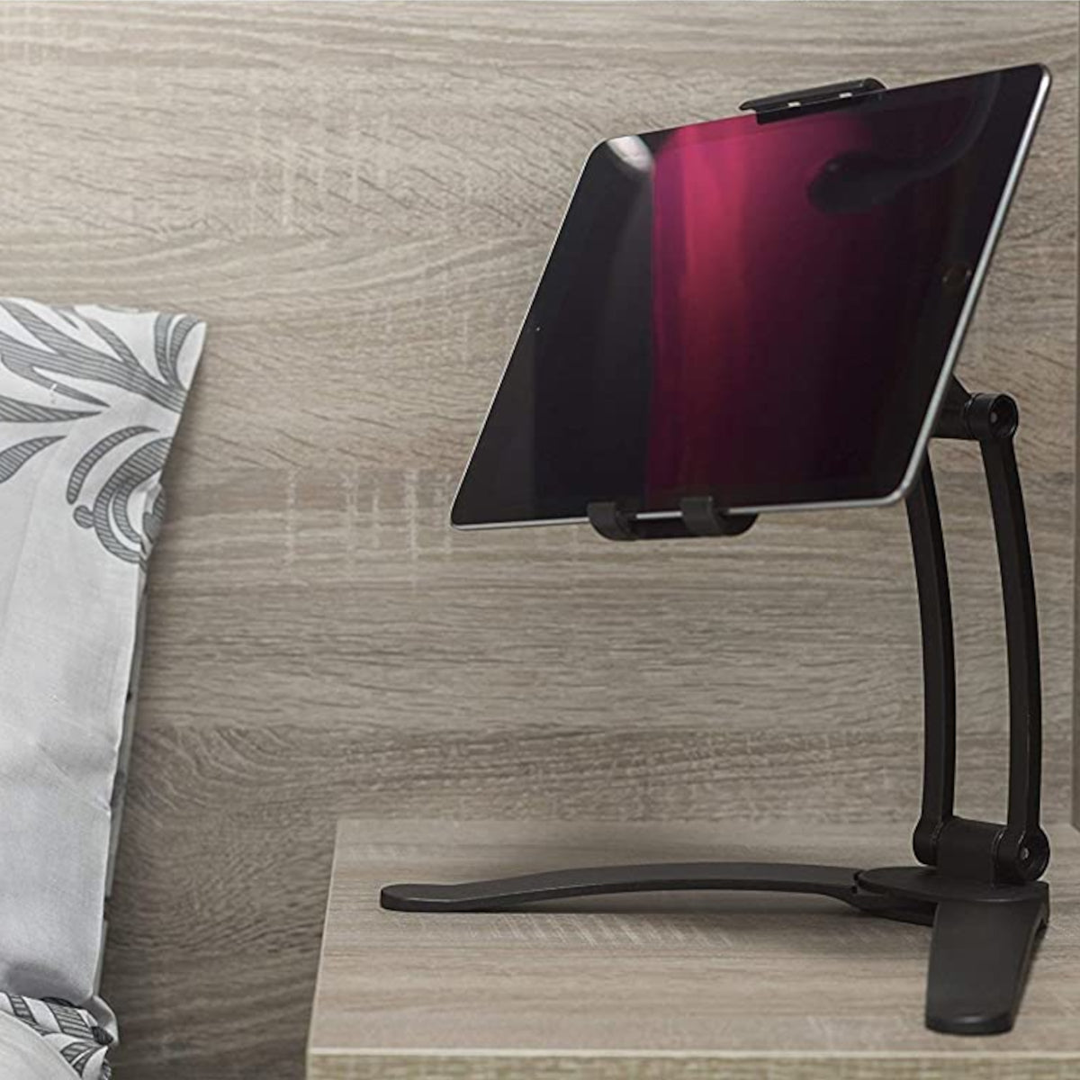 An Apple Ipad in a tablet stand on a bedside table in a bedroom with grey wood effect walls and table